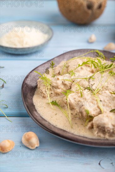 Stewed chicken fillets with coconut milk sauce and mizuna cabbage microgreen on blue wooden background. side view, close up, selective focus