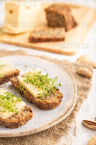 Grain bread sandwiches with cheese and watercress microgreen on gray concrete background and linen textile. side view, close up, selective focus