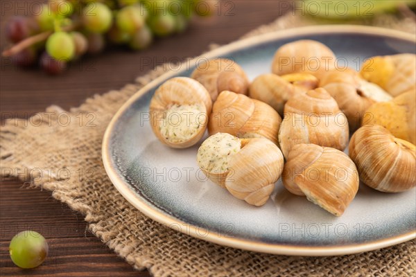 Grape (Burgundy) snails with butter and cheese on brown wooden background and linen textile. Side view, selective focus