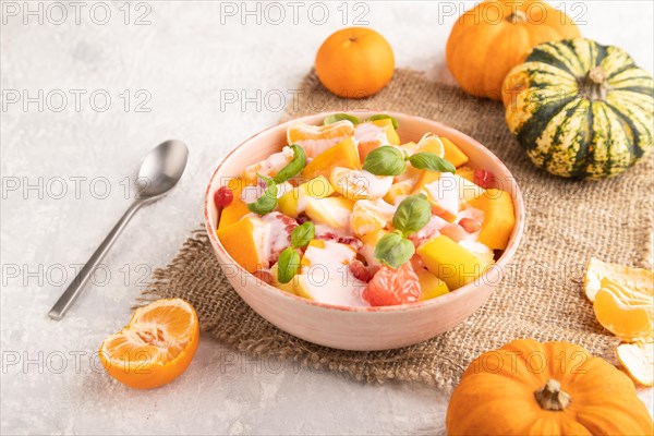 Vegetarian fruit salad of yogurt pumpkin, tangerine, pomegranate, grapefruit, basil microgreen sprouts on gray concrete background and linen textile. Side view, close up