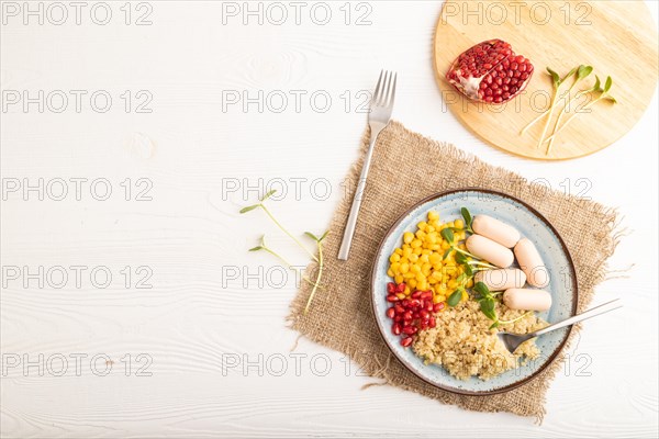 Mixed quinoa porridge, sweet corn, pomegranate seeds and small sausages on white wooden background. Top view, flat lay, copy space. Food for children, healthy food concept