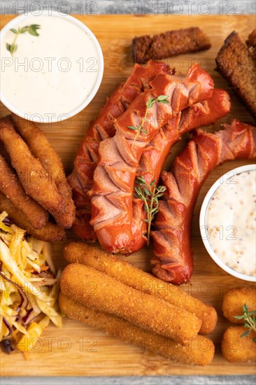 Set of snacks: sausages, nuggets, cheese sticks, toast, cabbage salad on a cutting board on a gray wooden background. Top view, flat lay, close up