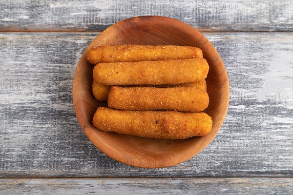 Heap of cheese sticks on a wooden plate on a gray wooden background. Top view, flat lay, close up