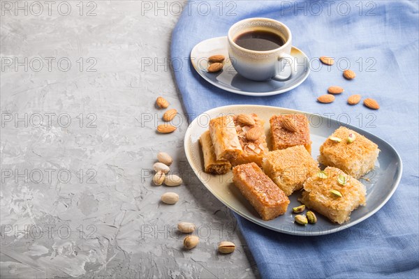 Traditional arabic sweets (basbus, kunafa, baklava) and a cup of coffee on a gray concrete background and blue textile. side view, copy space