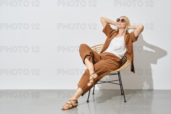 Relaxed blonde woman leans back in a wicker chair with her hands behind her head