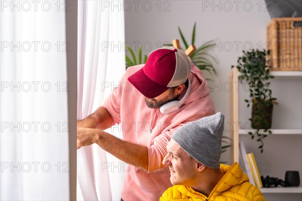 Curious disabled man and friend looking through the window from inside a warm living room