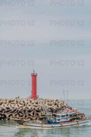 Small fishing trawler passing in front of red lighthouse as it enters harbor in South Korea