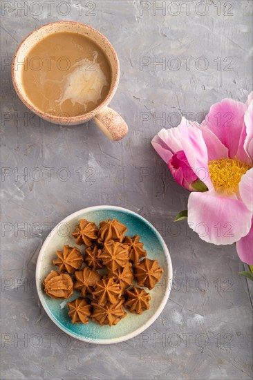 Homemade soft caramel fudge candies on blue plate and cup of coffee on gray concrete background, peony flower decoration. top view, flat lay, close up