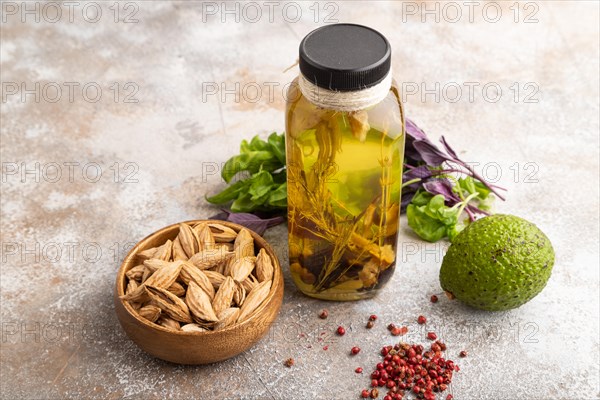 Sunflower oil in a glass jar with various herbs and spices, sesame, rosemary, avocado, basil, almond on a brown concrete background. Side view, copy space