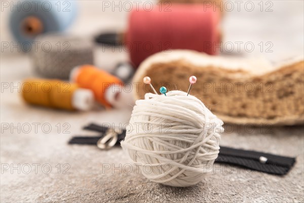 Sewing accessories: scissors, thread, thimbles, braid on brown concrete background. Side view, close up, selective focus