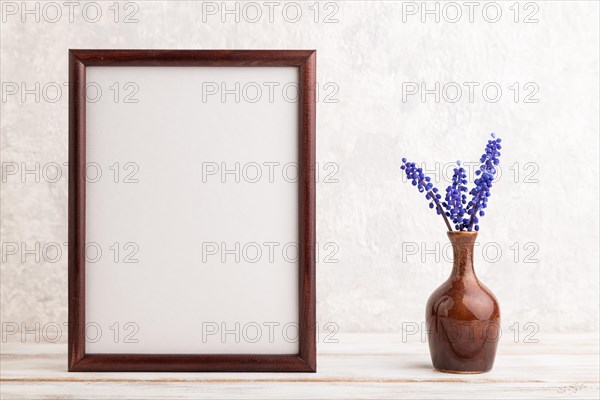 Wooden frame with blue muscari hyacinth flowers in ceramic vase on gray concrete background. side view, copy space, still life, mockup, template, spring, summer minimalism concept