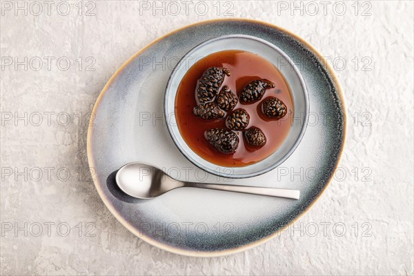 Pine cone jam on ceramic plate on gray concrete background. Top view, flat lay, close up