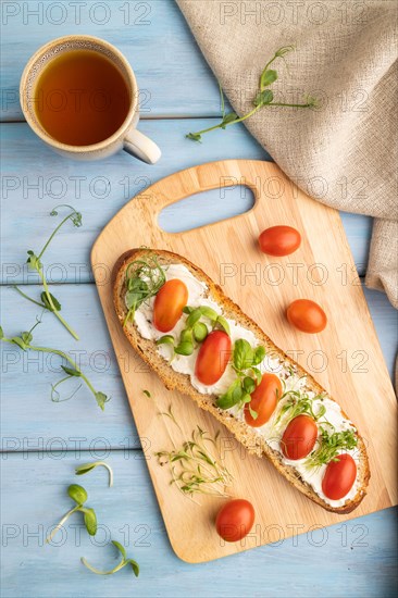 Long white bread sandwich with cream cheese, tomatoes and microgreen on blue wooden background and linen textile. top view, flat lay, close up