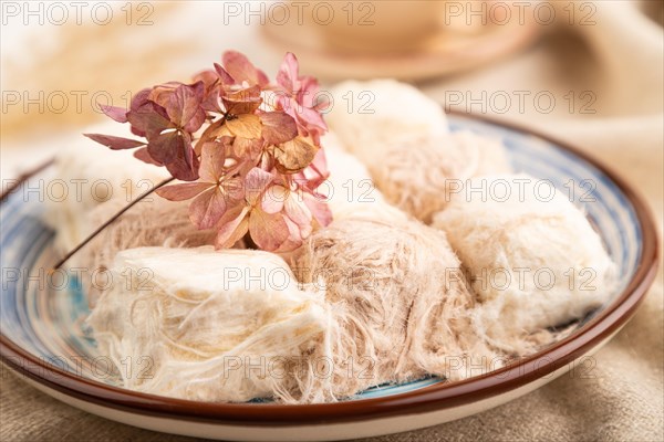 Traditional arabic sweets pishmanie and a cup of green tea on white wooden background and linen textile. side view, close up, selective focus