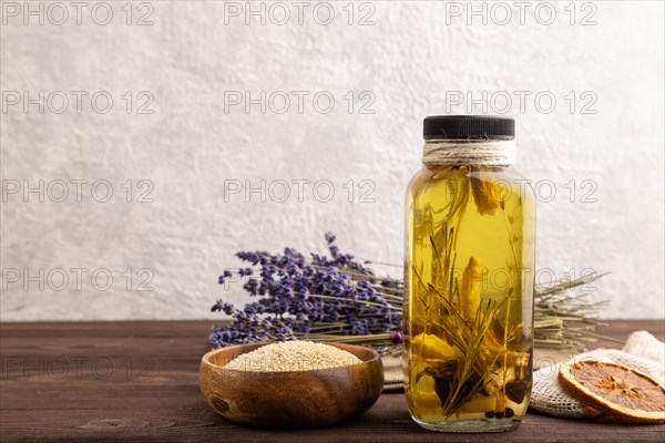 Sunflower oil in a glass jar with various herbs and spices, lavender, sesame, rosemary on a brown wooden background. Side view, copy space