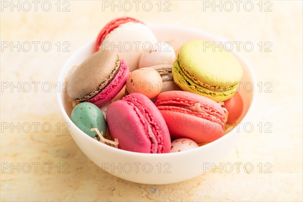 Multicolored macaroons and chocolate eggs in ceramic bowl on beige concrete background. side view, close up, still life. Breakfast, morning, concept