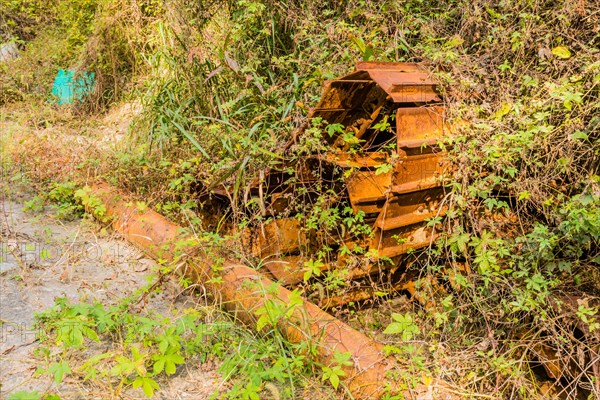 Broken and rusted tracks from old bulldozer covered with vines and weeds on hillside in wilderness