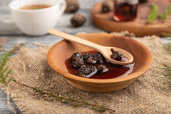 Pine cone jam with herbal tea on gray wooden background and linen textile. Side view, close up, selective focus