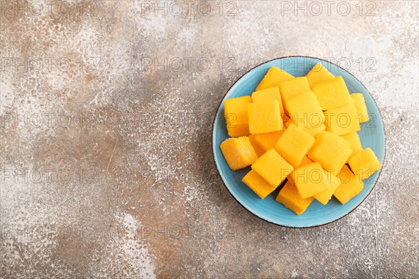 Dried and candied mango cubes on blue plate on brown concrete background. Top view, flat lay, copy space, vegan, vegetarian food concept