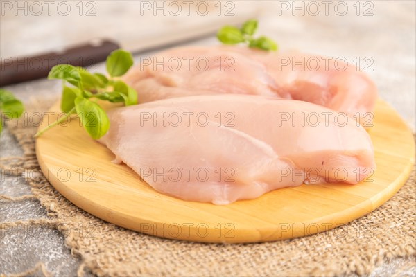 Raw chicken breast with herbs and spices on a wooden cutting board on a brown concrete background. Side view, close up, selective focus