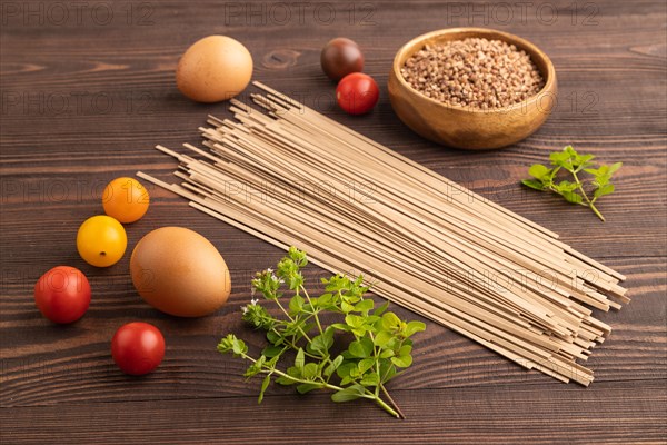 Japanese buckwheat soba noodles with tomato, eggs, spices, herbs on brown wooden background. Side view, close up
