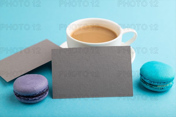 Gray paper business card mockup with blue and violet macaroons and cup of coffee on blue pastel background. Blank, side view, copy space, still life, close up. morning, breakfast concept