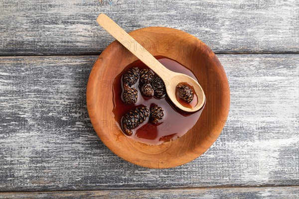 Pine cone jam in wooden bowl on gray wooden background. Top view, flat lay, close up