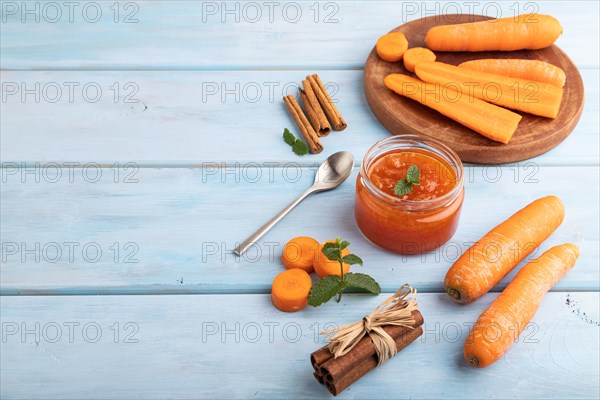Carrot jam with cinnamon in glass jar on blue wooden background. Side view, copy space