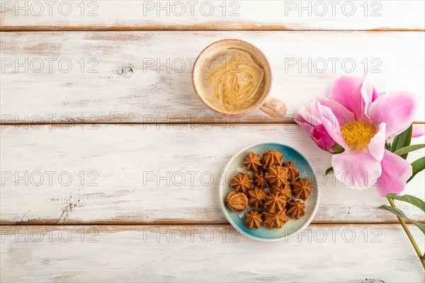 Homemade soft caramel fudge candies on blue plate and cup of coffee on white wooden background, peony flower decoration. top view, flat lay, copy space