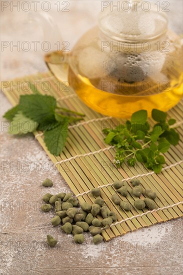 Green oolong tea with herbs in glass on brown concrete background. Healthy drink concept. Side view, close up, selective focus