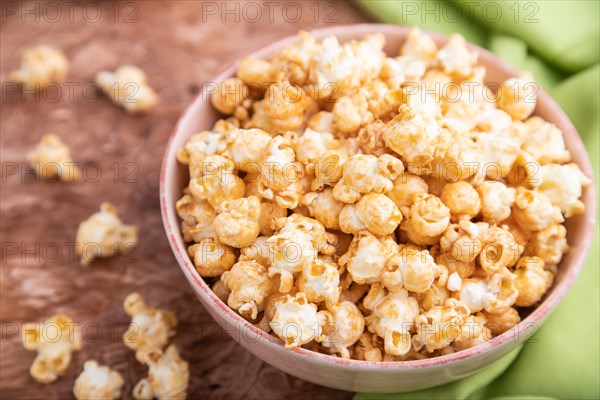 Popcorn with caramel in ceramic bowl on brown concrete background and green textile. Side view, close up, selective focus