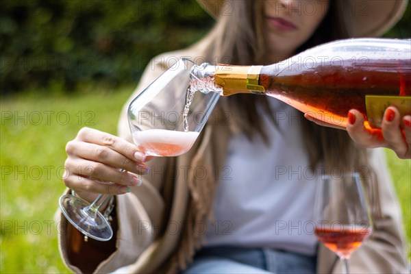 Unrecognizable woman holding a glass cup while being served some red champagne outdoors in the park