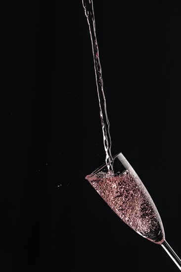 A champagne glass catches rose sparkling wine against a dark background