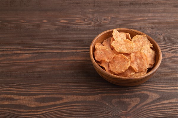 Slices of dehydrated salted meat chips with herbs and spices on brown wooden background. Side view, copy space