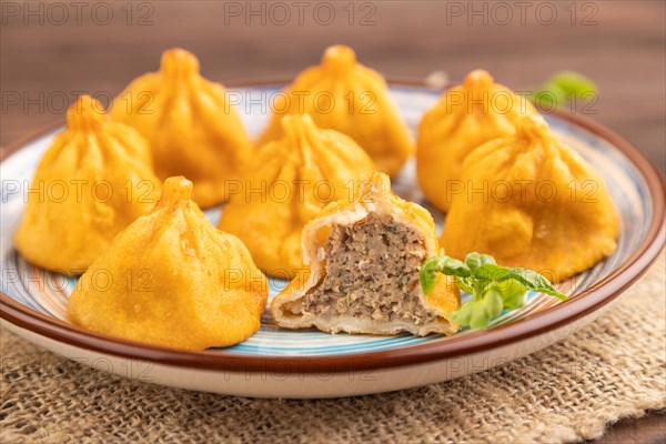 Fried manti dumplings with pepper, basil on brown wooden background and linen textile. Side view, close up, selective focus