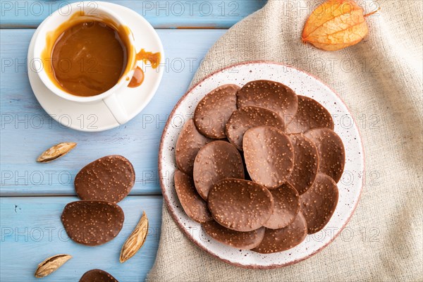 Chocolate chips with cup of coffee and caramel on a blue wooden background and linen textile. top view, flat lay, close up