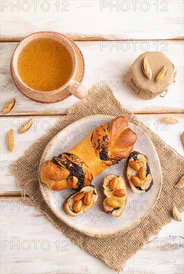 Homemade sweet bun with honey almonds and cup of green tea on a white wooden background and linen textile. top view, flat lay, close up