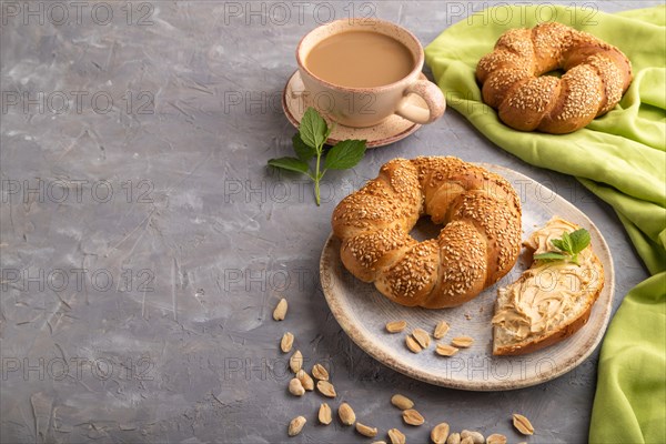 Homemade sweet bun with peanut butter and cup of coffee on a gray concrete background and green linen textile. side view, copy space