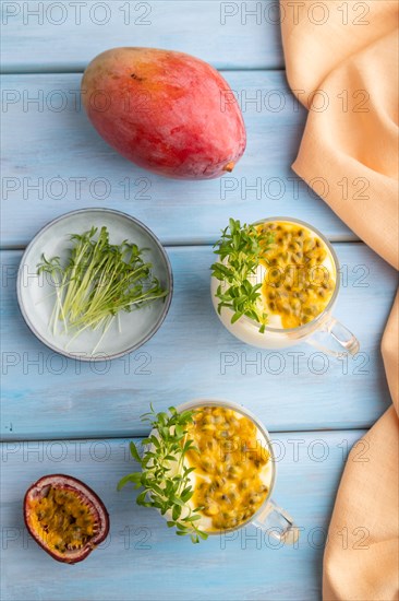 Mango yogurt with passionfruit and cilantro microgreen in glass on blue wooden background with orange linen textile. Top view, flat lay, close up