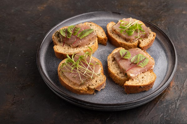 Bread sandwiches with jerky salted meat, sorrel and cilantro microgreen on black concrete background. side view, close up