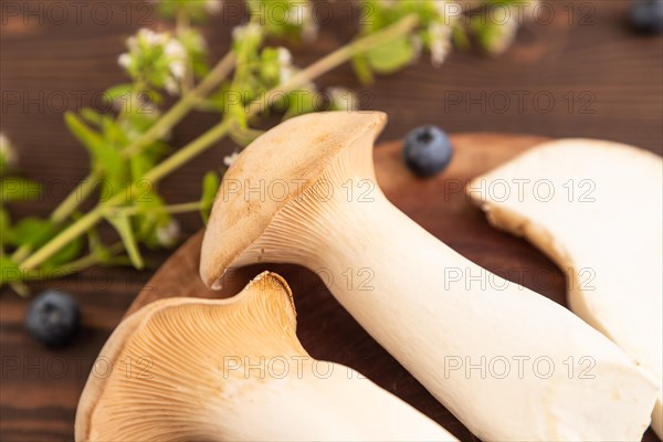 King Oyster mushrooms or Eringi (Pleurotus eryngii) on brown wooden background with blueberry, herbs and spices. Side view, selective focus
