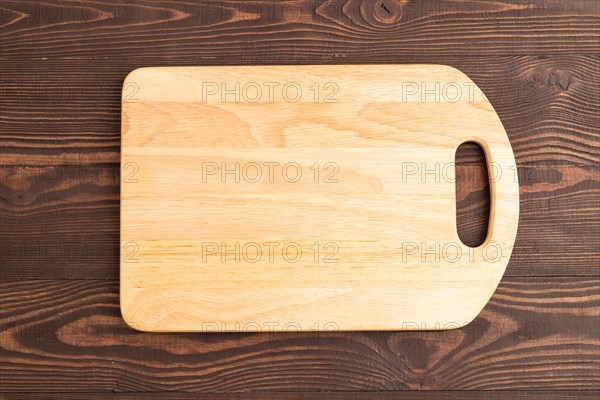 Empty rectangular wooden cutting board on brown wooden background. Top view, close up, flat lay