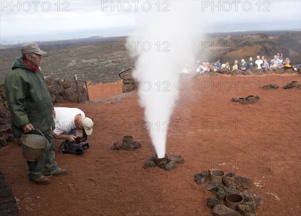 Tourists watch steam rise from geyser spout, Parque Nacional de Timanfaya, national park, Lanzarote, Canary Islands