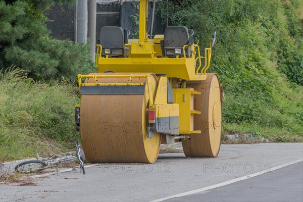 Bicycle laying abandoned in street in front of large road roller in wooded countryside