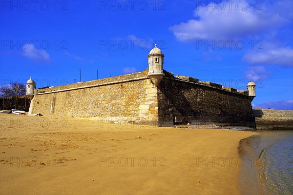 Golden sand on the beach at Lagos, with the old harbour defenses, the 17th century Forte Bandeira, under a deep blue sky, Algarve, Portugal, Europe