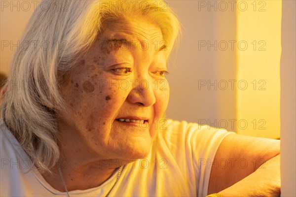 Senior adult woman looking out the window and smiling. Bright environment. Older adult woman looking out the window with a happy expression on her face