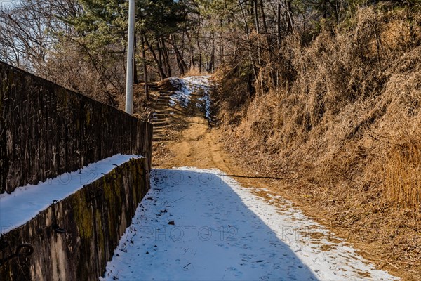 Snow covered hiking trail beside concrete wall in wilderness park in South Korea