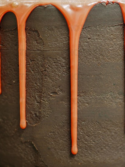 Close-up of an orange icing drizzle on the side of a chocolate cake