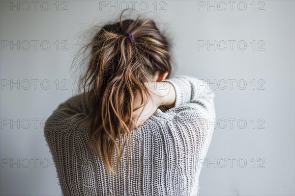 A girl from behind, visibly pensive, with a bun in her hair and holding her neck, symbolising depression and abuse, AI generated, AI generated