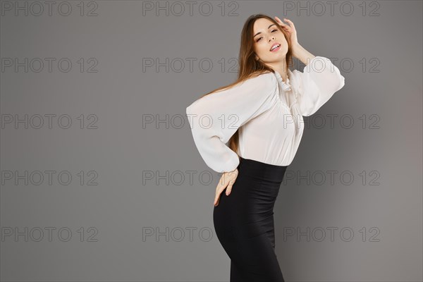 Gorgeous young woman in pencil skirt and blouse posing in grey studio